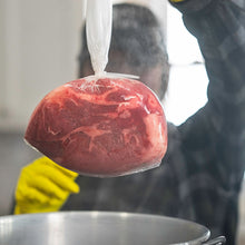 Load image into Gallery viewer, Bag of meat being removed from a pot of water
